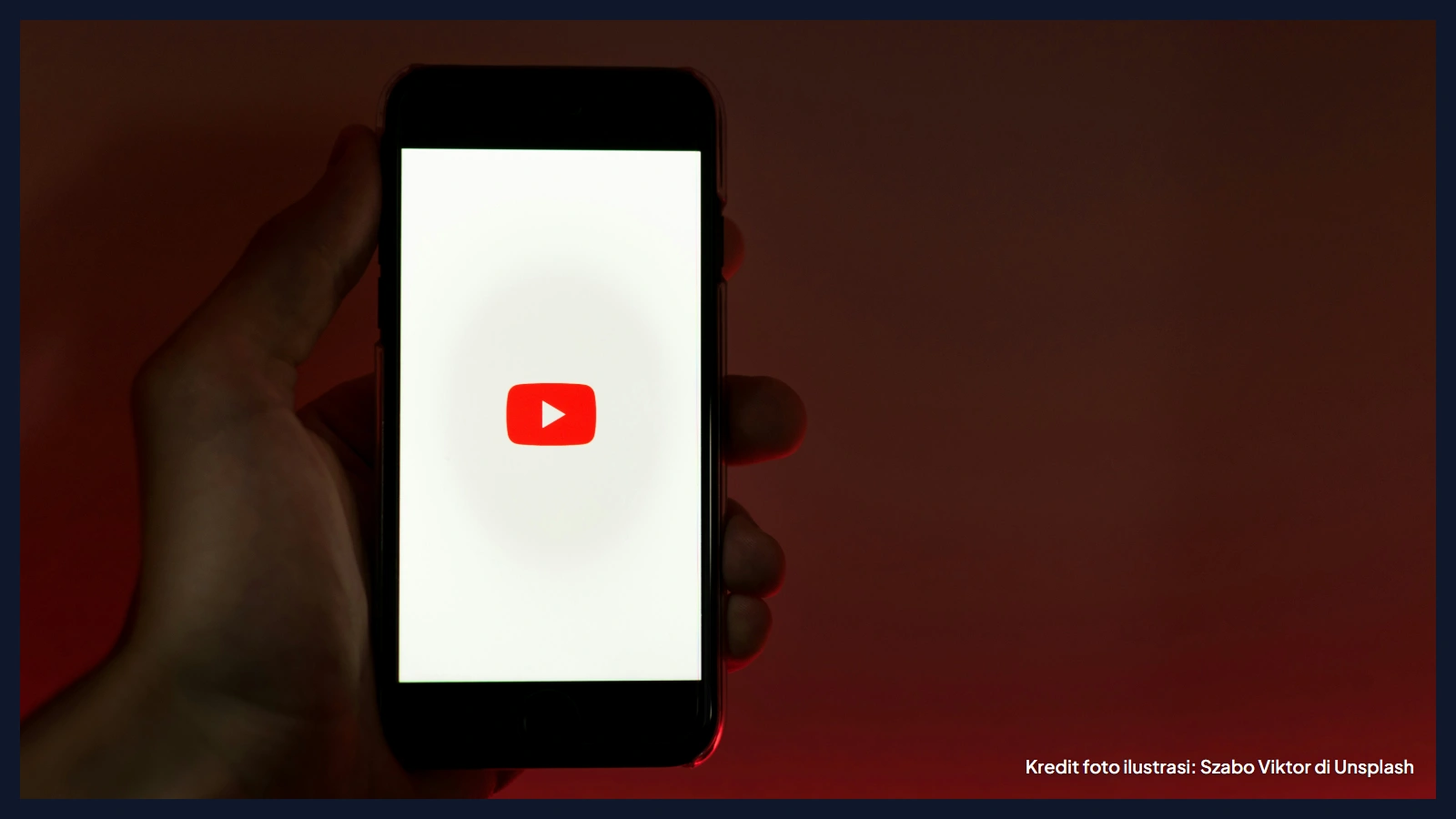 Tangan memegang ponsel yang menampilkan logo YouTube di layar dengan latar merah gelap